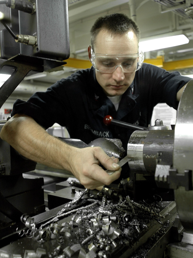 Ein Maschinenbediener mit Schutzbrille bedient eine Maschine in einer hell erleuchteten Fabrikumgebung.