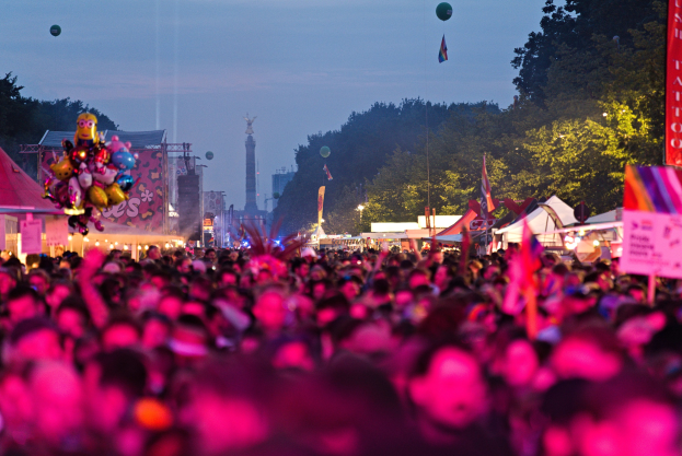Eine große Menschenmenge auf einem nächtlichen Musikfestival mit bunten Lichtern, Ballons, Zelten, Bannern, Fahnen, Bäumen, einem Turm und einem sternenklaren Himmel im Hintergrund.
