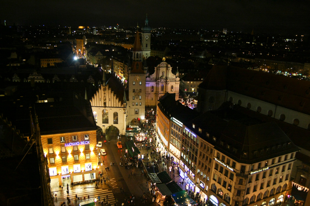 Eine Vogelperspektive auf eine Stadt bei Nacht, die zahlreiche Gebäude, Häuser, Straßen voller Fahrzeuge und Menschen zeigt.