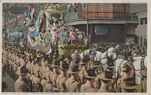 Eine alte Postkarte zeigt einen Mardi Gras-Umzug in New Orleans mit einem geschmückten Float, Menschen auf Pferden und Zuschauern am Straßenrand, mit der Beschriftung "The Rex Float, Mardi Gras Carnival, New Orleans" am unteren Rand.