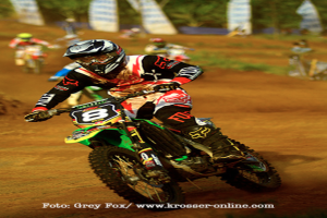 Mehrere Personen bei einem Motorradrennen, alle mit Helmen, mit Text am unteren Bildrand.