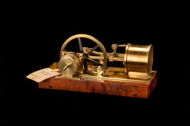 Altmodische Uhr mit Holzunterteil, Metallrad und Papier-Zeitschalt-Anschluss auf schwarzem Hintergrund.