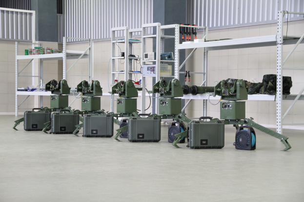 Gruppe von Militärrobotern auf einem Boden mit Koffern und Objekten auf Gestellen, in der Nähe einer Wand und eines Geländers, Teil eines Verteidigungssystems.