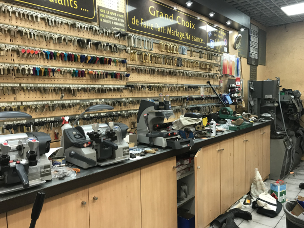 Ein unordentlicher Garage-Workshop voller verschiedener Werkzeuge, Maschinen, Schränke und Gegenstände auf dem Boden, einschließlich Bretter mit Text, eine Wanduhr und Deckenleuchten.