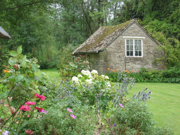 Ein Haus umgeben von Pflanzen und Bäumen auf einer grünen Wiese.