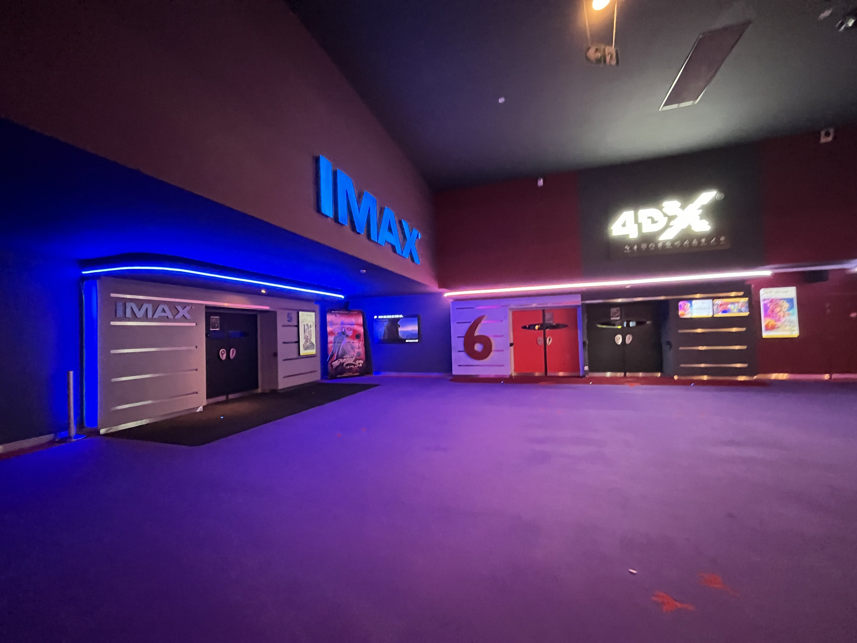 Ein Kinosaal mit einem lila Teppichboden, textgeschmückten Wänden, Bildschirmen und einer beleuchteten Decke.