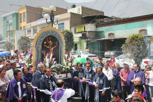Menschen auf einer Straße mit einem Kreuz und Blumensträußen in der Mitte, Autos im Hintergrund und Gebäude, Bäume und Straßenlaternen weiter hinten.