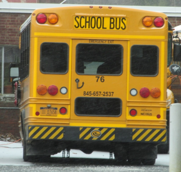 Ein gelber Schulbus steht vor einem Backsteinbau mit Fenstern.
