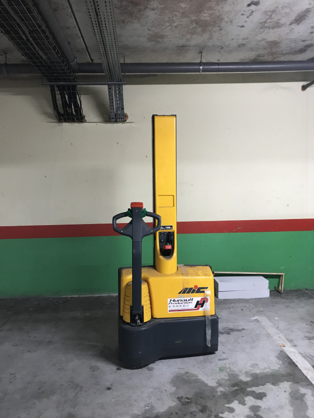 Ein gelber Gabelstapler in einem Lager mit Metallregalen auf der linken Seite und einer Wand im Hintergrund geparkt.