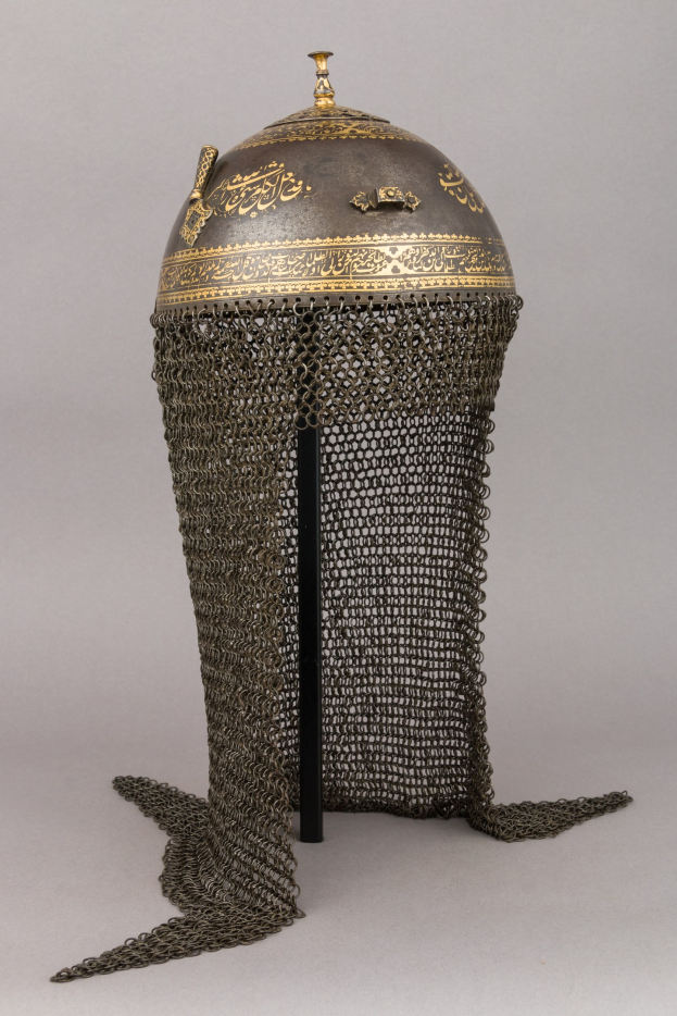 Schwarzer und goldener Kettenhemdhelm mit detaillierten königlichen Elementen auf einem Sockel vor einem weißen Hintergrund.