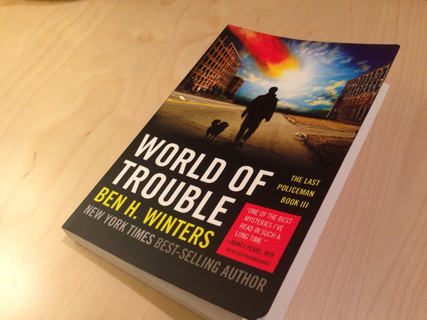 Ein Buch mit dem Titel "World Of Trouble", das einen Mann und einen Hund auf dem Cover zeigt, liegt auf einem Tisch.