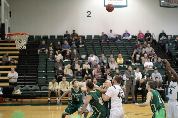 Ein Basketballfeld mit aktiv spielenden Spielern und Zuschauern im Hintergrund, die das Spiel verfolgen.