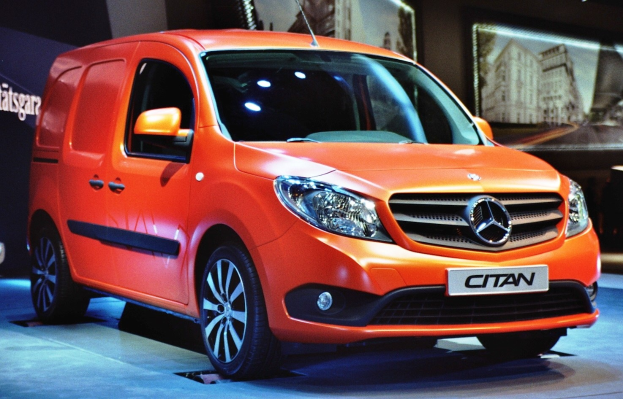 Orangefarbener Mercedes-Benz Citan Van auf einer Automesse umgeben von moderner schwarzer Schlafzimmermöblierung.
