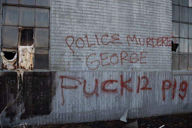 Ein Gebäude mit der Aufschrift "Polizei mörder George Fuck 12 P19" auf der Seite, das Fenster und verschiedene Gegenstände vorne zeigt.