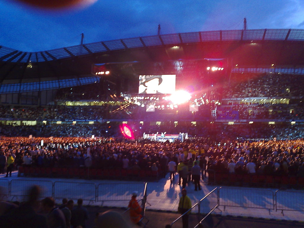 Ein Konzertsaal mit Menschen, Scheinwerfern und einem Projektionsschirm.