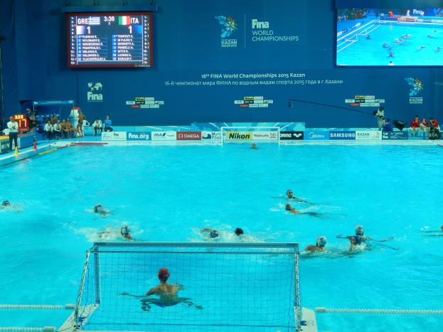 Wasserballspieler bei den 2016 FINA-Weltmeisterschaften in Kazan im Pool gegeneinander antretend, mit Zuschauern und Anzeigetafel im Hintergrund.