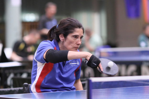 Eine Frau hält einen Schläger, spielt mit einem Ball, mit einer Platte und Netz im Hintergrund.