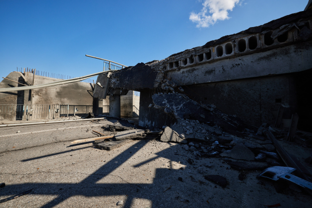 Teilweise abgerissenes Gebäude inmitten einer Straße, mit Trümmern drumherum, Straße im Vordergrund und bewölkter Himmel im Hintergrund.