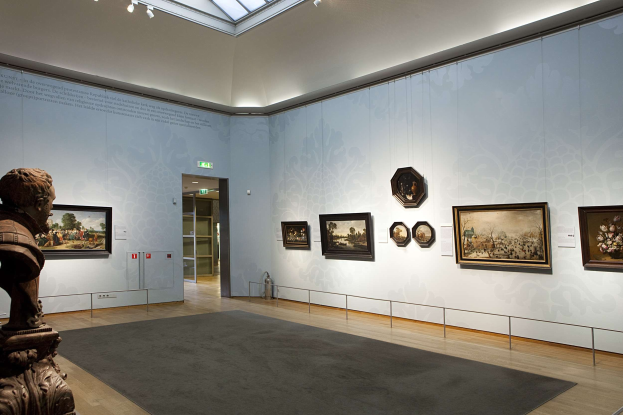 Ein prächtiger Museumsraum mit einer Statue links, einem Teppichboden, Fotorahmen an den Wänden, einer Glasdecke mit Lichtern und Türen im Hintergrund.