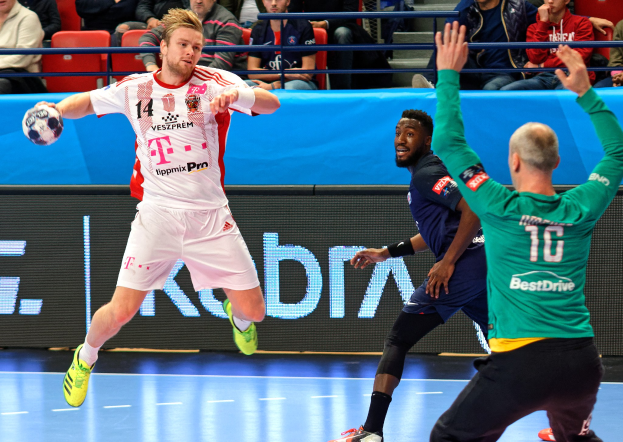 Eine Gruppe von Männern, die auf einem Feld Handball spielen, mit einem Ball in der Mitte, während Zuschauer von Stühlen und Geländern in einer Arena zuschauen, mit einem Schild, auf dem "Futsal-Weltmeisterschaft 2019 - Bayern München gegen Paris Saint-Germain" steht.