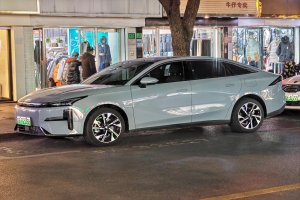 Ein Mitsubishi Lancer EV Elektroauto, das nachts auf einer Straße geparkt ist, umgeben von Gebäuden, Geschäften, Schaufensterpuppen mit Kleidern, Schildern, Lichtern und anderen Gegenständen.